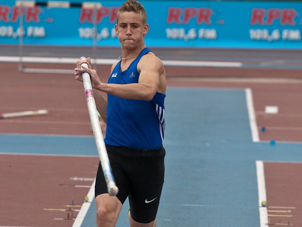 boy in blue uniform with pole in his hands is about to extend both his hands above his head while pole vaulting