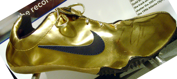 track spikes shoes that are gold in color and have a solid black swooshy Nike sign on the side
